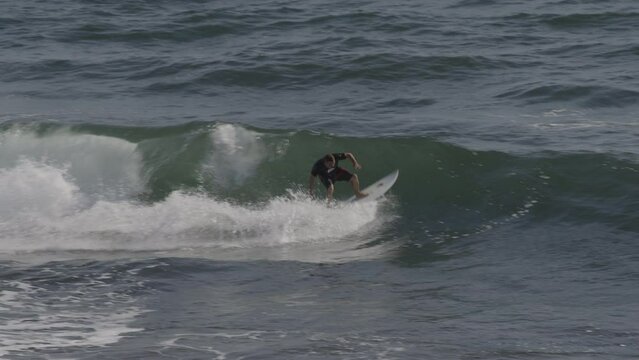 Slow motion tracking shot of distant man surfing on ocean wave / El Tunco, La Libertad, El Salvador