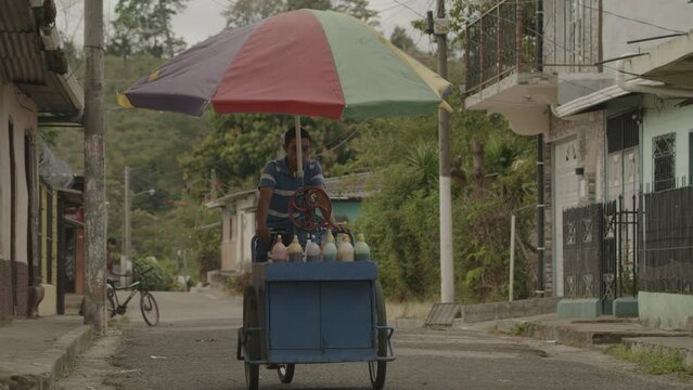 Man pedaling mobile snow cone food cart in city street / Tamanique, La Libertad, El Salvador
