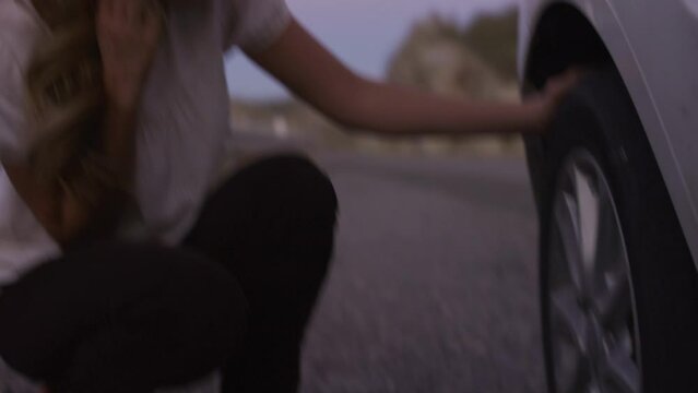Close up of woman inspecting flat tire on car at night / Nephi, Utah, United States