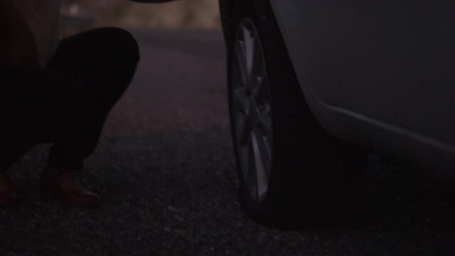 Close up of woman inspecting flat tire on car at night / Nephi, Utah, United States