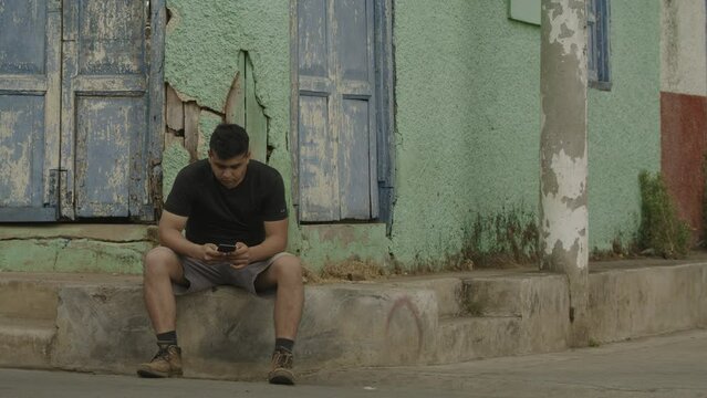 People passing man sitting on city corner texting on cell phone / Tamanique, La Libertad, El Salvador