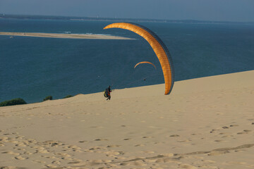 Single paraglider with parachute at the dune of Pilat on a sunny day, Arcachon, Nouvelle-Aquitaine, France - obrazy, fototapety, plakaty