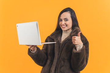 Young adult latin american woman wearing brown fur coat holding up laptop and looking to camera...