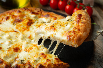 A slice of hot Italian pizza with stretching cheese. Pizza four cheeses with basil.