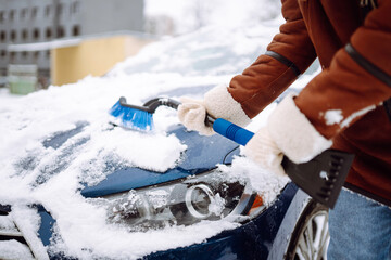 Young woman cleaning snow from car with brush. Transport, winter,  people and vehicle concept.