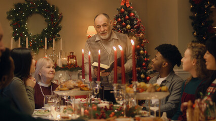 Drandfather reads Bible on family Christmas dinner. Happy large family praying before celebrating...