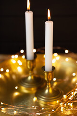 Candles in bronze candlesticks on a golden stand. Black wooden background. Candle lights and led flashlights