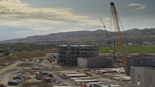 Aerial flyover view of cranes at construction site near mountain range / Riverton, Utah, United States