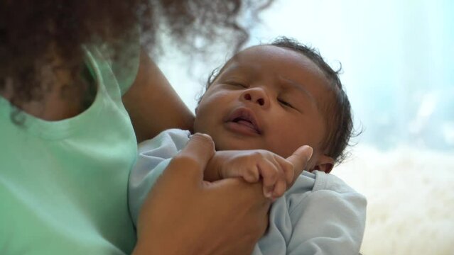 Portrait of African newborn baby one-month-old cheerful curious sleep in warm embrace of motherhood. Mother playful holding Adorable little infant son develop, with, Mum and child tender moments.
