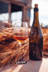 a glass of amber wine and a bottle of wine near a sheaf of wheat