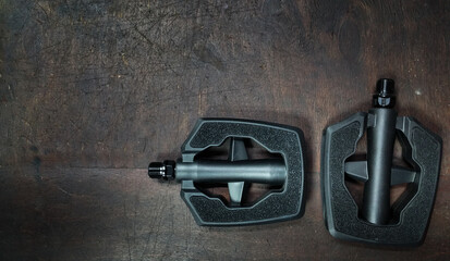 two black plastic Flat Pedal for the city bike on a dark wooden background top view