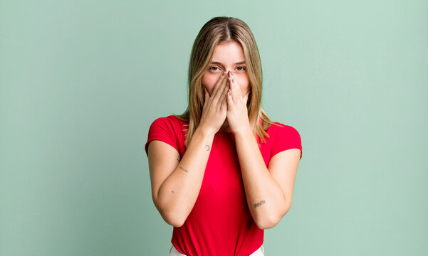 blonde pretty woman covering mouth with hands with a shocked, surprised expression, keeping a secret or saying oops