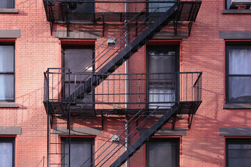Close up New York City apartment building painted red brick exterior, windows, and diagonal fire...