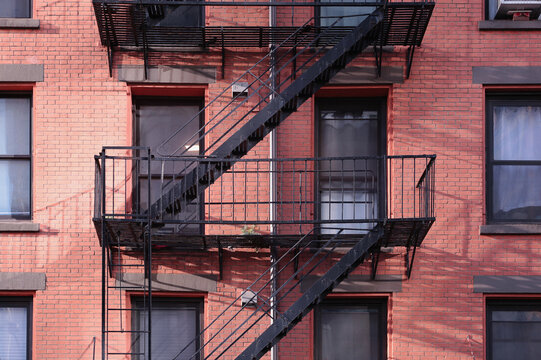 Close up New York City apartment building painted red brick exterior, windows, and diagonal fire escape stairs