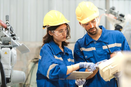 Male Industrial Engineer Using Remote Control Board To Check Robotic Welder Operation In Modern Automation Factory. Woman Technician Monitoring Robot Controller System For Automated Steel Welding.