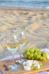 Glasses with white wine and snacks for beach picnic on sandy seashore