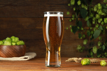 Glass of beer, fresh green hops and spikes on wooden table
