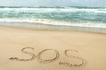 Message SOS drawn on sand near wavy sea