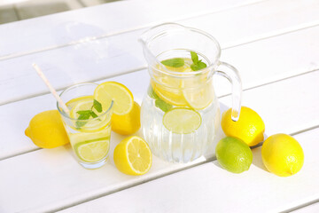 Water with lemons and limes on white wooden table outdoors