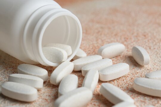 White medical bottle and pills on color textured surface, closeup