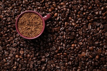 Cup with instant coffee on roasted beans, top view. Space for text