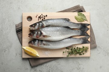 Tasty sea bass fish and spices on grey textured table, top view