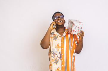 Young smiling African American male with glasses making a phone call, holding a gift box in his hand