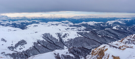Panoramic aerial view of Caucasus Mountain Range from Gum Bashi pass on cloudy winter day. Karachay-Cherkessia, Russia.