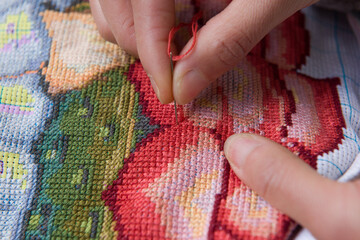 Woman hands working cross-stitch. A close up of embroidery. - obrazy, fototapety, plakaty