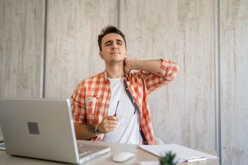 young man stretching at work while sitting at desk having neck pain