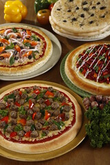 Various flavors of pizza with ingredients on a wood table