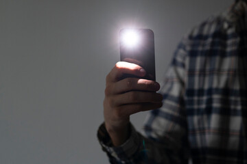 hand holding a smartphone used as a torched, flashlight of mobile phone in the dark - obrazy, fototapety, plakaty
