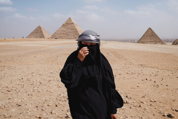 Woman muslim with robe clothes walks on the background of the pyramids in Giza, Egypt