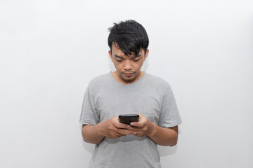 Asian young man rubs his eye and looks at smartphone after wake up from sleep with white background