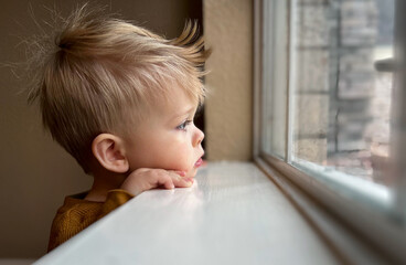 Cute little toddler looking at the window at home, close up portrait 