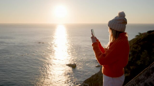 Woman taking pictures of postcard, panoramic scenery with sunset skyline in the background. Female tourist exploring beautiful setting of the pristine, coastal area. High quality 4k footage