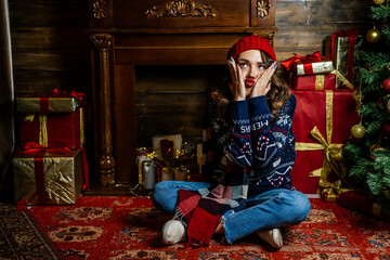 A beautiful brunette sits under a Christmas tree against the backdrop of New Year's decorations.