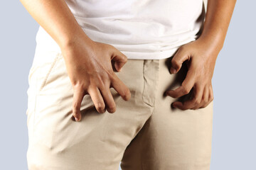 Asian man in reaction of scratching crotch on grey background, closeup. Annoying itch or Tinea Cruris. Human body problem or healthcare and medicine concept.