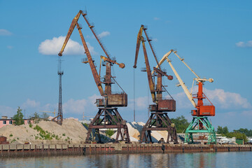 Fototapeta na wymiar Three port cranes in the river port on a sunny summer day