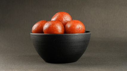Sweet Gulab Jamun served in black ceramic bowl, Famous Indian dessert sweets isolated over black indoor studio background