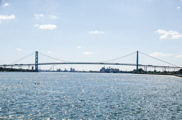 The Ambassador Bridge connects Detroit, Michigan, and Windsor Ontario over the Detroit river.  Taken from West Riverfront Park in the daytime on a mostly clear day. Waves can be seen in the river..