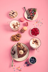 Table with various cookies, donuts, cakes, coffee cups on pink background.