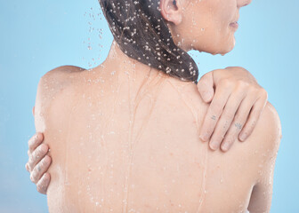 Back, woman and shower for skincare, clean and hygiene against blue studio background. Young female, girl and liquid drops for washing, body care or natural beauty for wellness, water splash or relax