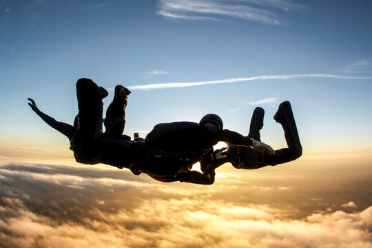 Skydiving freefall silhouette of four people in formation, teamwork concept at sunset