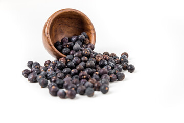 Juniper berries spilling from a wood bowl isolated over white focus on bowl