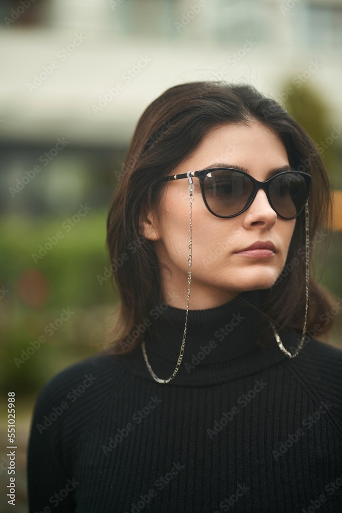 Sticker A gorgeous brunette woman wears sunglasses with sunglasses chains. Confident girl in urban portrait.