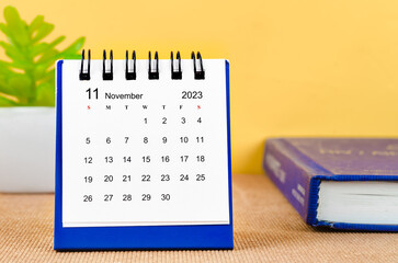 The November 2023 Monthly desk calendar for 2023 with a book on yellow background.