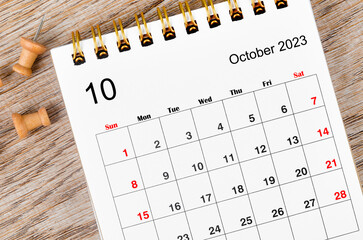 The October 2023 Monthly desk calendar for 2023 year with pin on wooden background.