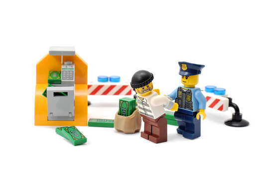 Lego minifigures of fighting criminal and police officer are standing in front of cashpoint. Editorial illustrative image of law and punishing. Studio shot.
