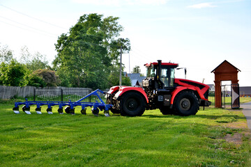 red tractor with black wheels and blue plow isolated on green grass, close-up